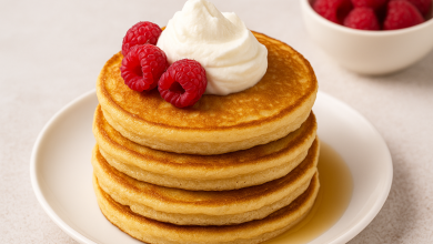 Stack of keto coconut flour pancakes topped with whipped cream and raspberries on a white plate