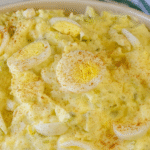 Old-fashioned potato salad topped with sliced boiled eggs and paprika, served in a white bowl