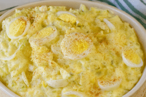 Old-fashioned potato salad topped with sliced boiled eggs and paprika, served in a white bowl