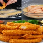 Golden fried crispy chicken strips stacked on a plate with dipping sauce and lemon wedges.