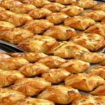 Golden brown mini puff pastry parcels filled with cheese and spinach on a baking tray