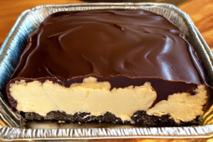 No-bake chocolate eclair cake with layers of graham crackers, vanilla pudding, whipped topping, and chocolate frosting in a pan