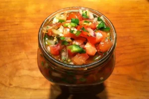 Fresh homemade Pico De Gallo salsa in a glass jar on a wooden table